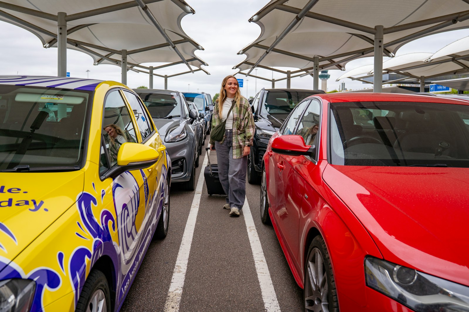 Reisende mit Koffer zwischen geparkten Autos
